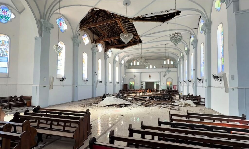 Interior da Paróquia Santa Quitéria, em Curitiba, com parte do teto desabado e destroços sobre os bancos.